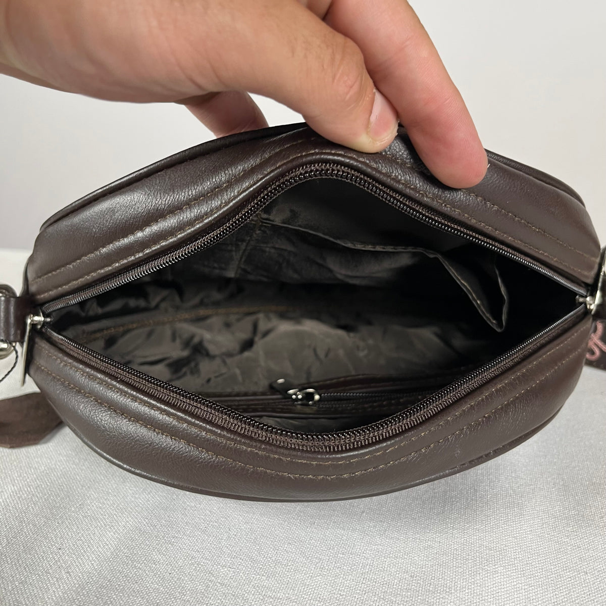 Brown leather circle bag shown with detachable embroidered sling